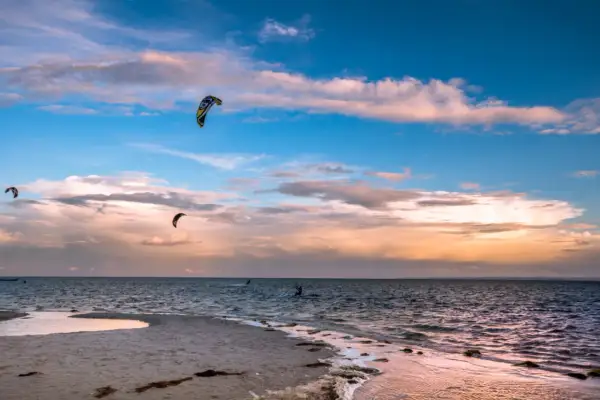 Zachód słońca nad Bałtykiem. Kilku śmiałków uprawia kitesurfing w Polsce, unosząc się na falach pod kolorowym niebem.