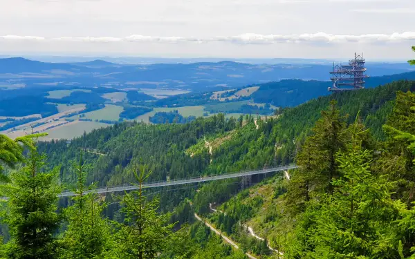 Widok na najdłuższy most Czech, zawieszony nad zieloną doliną. W oddali widać wieżę widokową.