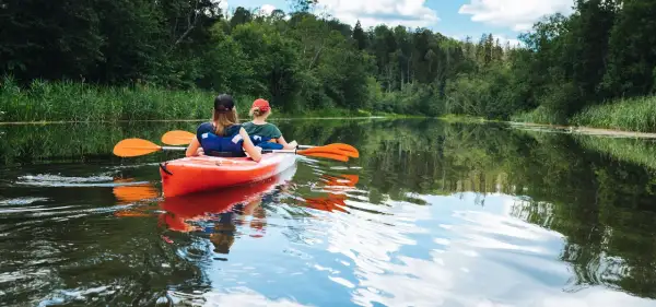 Dwie osoby płyną kajakiem po spokojnej rzece, ciesząc się pięknem przyrody. To idealny spływ kajakowy Mazury.