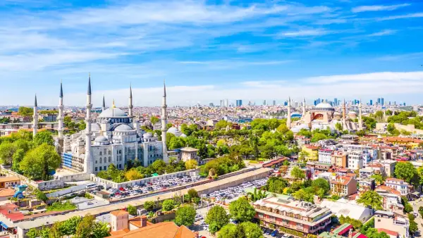 Widok na Stambuł, miasto łączące Europę i Azję, z Błękitnym Meczetem i Hagia Sophia. W tle nowoczesne wieżowce, a na pierwszym planie zielone drzewa i zabudowa miejska.