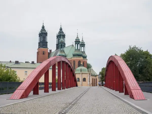 Czerwony most na poznańskiej trasie prowadzi do katedry. Spacerowicze podziwiają architekturę.