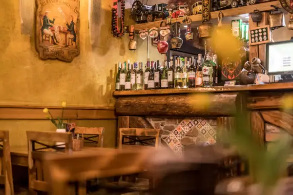 Drewniane stoły i krzesła w przytulnych restauracjach w Szklarskiej Porębie. Na półce rząd butelek wina, a nad nimi ozdoby.