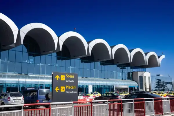 Nowoczesny terminal lotniska w Bukareszcie z charakterystycznymi łukami dachu. Tablice kierują do przylotów i odlotów.