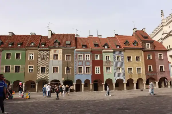 Kolorowe kamieniczki na poznańskim rynku, z arkadami i ludźmi spacerującymi po bruku.