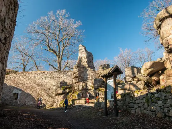 Ruiny zamku na Rudawach Janowickich, kamienne mury, skalne formacje i nagie drzewa pod błękitnym niebem.