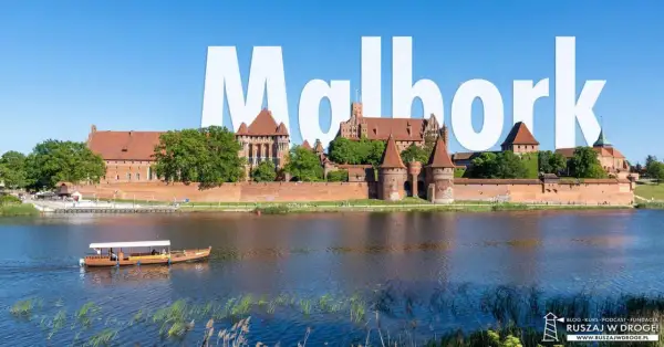 Majestatyczny zamek w Malborku, jedna z największych atrakcji Polski, widziany od strony rzeki Nogat. Stateczek wycieczkowy płynie po wodzie.